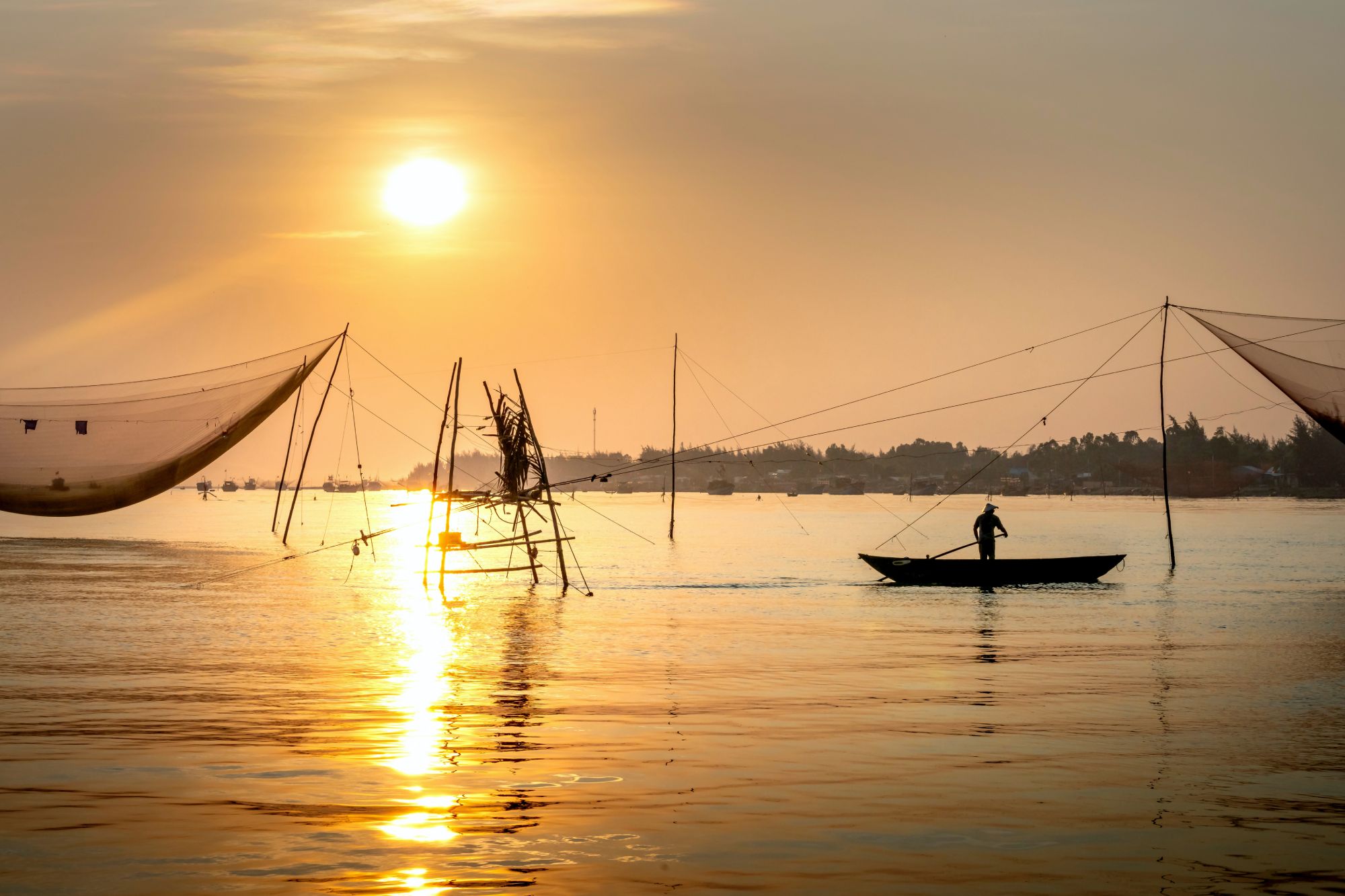 Person fishing on a boat at sunset; bamboo fishing poles