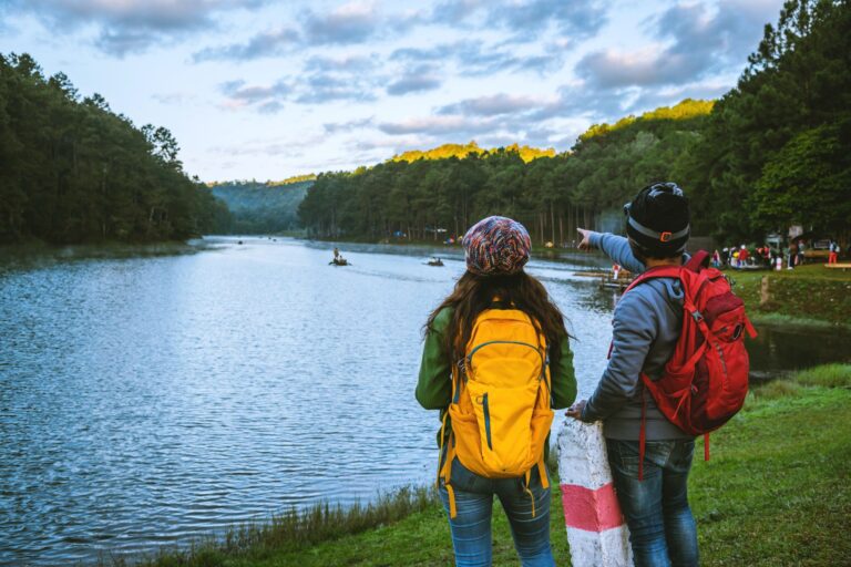 Couple wearing backpacks watching people canoeing on a lake; bamboo camping gear
